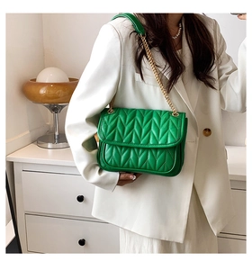 Detail of bright green quilted shoulder bag with gold chain strap on white blazer