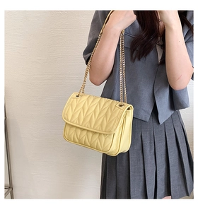 Detailed shot of yellow quilted shoulder bag with gold chain strap on female model
