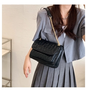 Detail of black quilted leather shoulder bag with gold chain strap on model