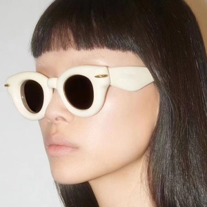 Détail de lunettes de soleil blanches épaisses avec accents dorés portées par un modèle