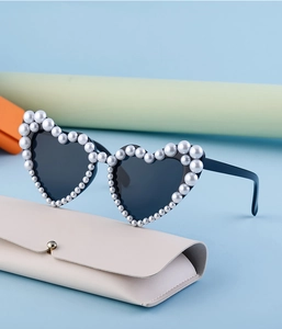Detail der herzförmigen Sonnenbrille mit perlenbesetztem Rahmen auf weißem Lederetui