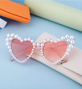 Detail einer herzförmigen Sonnenbrille mit rosa Glitzergläsern und künstlichen Perlen