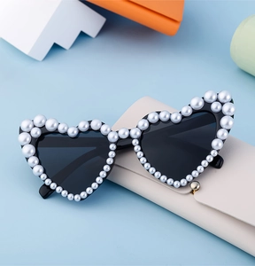 Detail einer herzförmigen Sonnenbrille mit Perlenbesatz und cremefarbener Lederhülle