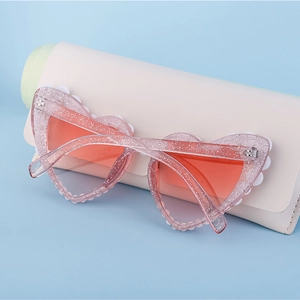 Nahaufnahme der herzförmigen Sonnenbrille mit rosa Glitzerrahmen und orangefarbenen Gläsern