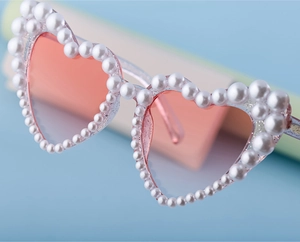 Nahaufnahme der herzförmigen Sonnenbrille mit Perlenrahmen und rosa Verlaufsgläsern