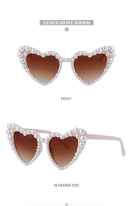 Detail einer herzförmigen Sonnenbrille mit cremeweißem Rahmen und künstlichen Perlen