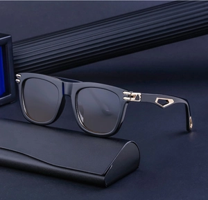 Square black sunglasses with gold metal accents and a leather case on a blue background