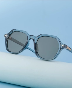 Close-up of light blue geometric sunglasses with gold metal hinge detail on a stand
