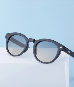 Detail of oval black sunglasses with gold arrow studs and blue gradient lenses
