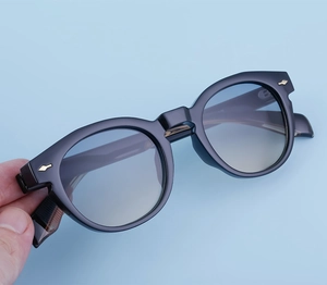 Detailed close-up of retro oval sunglasses featuring golden arrow accents and blue lenses