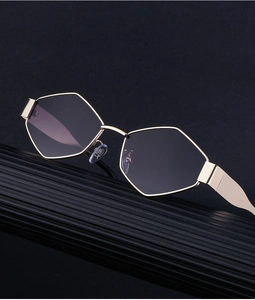 Détail de lunettes de soleil à monture polygonale dorée et verres dégradés sur support noir