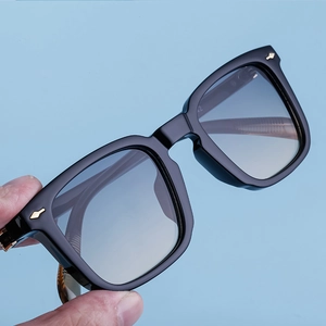 Detail of black square sunglasses with gradient lenses and gold arrow metal accents