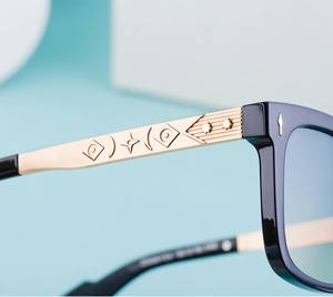 Detailed close-up of square sunglasses with gold metal temples and embossed geometric patterns