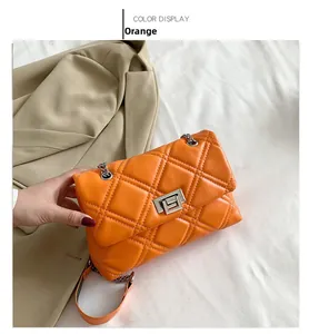Close-up of orange quilted chain bag with silver clasp on a beige blazer background