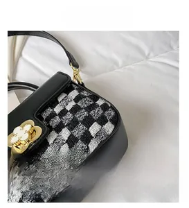 Detail of tweed houndstooth fabric and golden clover lock on black leather handbag