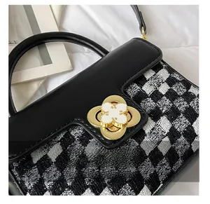 Detail showing golden clover rotary lock on black and white checkered woven handbag