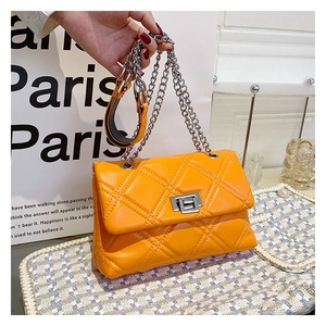 Close-up of bright orange quilted crossbody bag with silver twist lock and chain strap