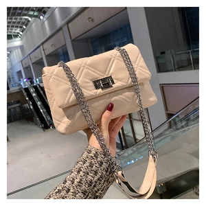 Close-up of beige quilted chain bag with silver swivel lock held by a hand