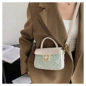 Detail of green tweed crossbody bag with golden clover clasp worn by model in brown blazer