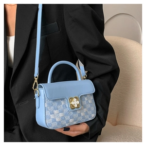 Close-up of light blue tweed handbag with golden flower clasp and woven texture detail