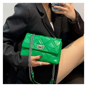 Close-up of bright green quilted shoulder bag with silver metal chain on black suit