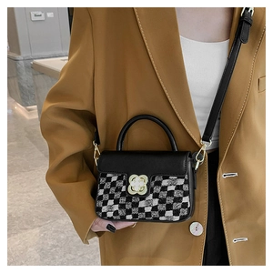Chic black and white checkerboard crossbody bag with gold clover clasp worn on an oversize blazer