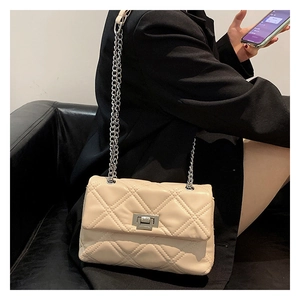 Close-up of quilted cream crossbody bag with silver twist lock and chain strap on model