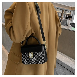 Detailed side view of a black leather crossbody bag featuring a golden flower clasp
