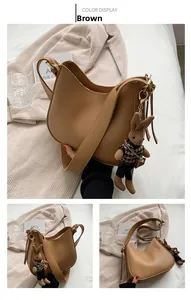Detail view of brown leather crescent tote bag with a cute rabbit doll charm