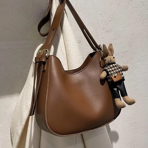 Brown leather half-moon shoulder bag with a cute knitted rabbit pendant and adjustable strap