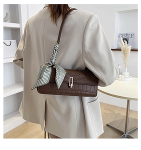 Dettaglio borsa baguette marrone effetto coccodrillo con foulard e fibbia dorata