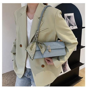 Dettaglio borsa celeste con trama a coccodrillo e foulard di seta a righe sulla tracolla
