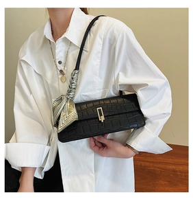 Détail du sac baguette noir texture croco avec boucle dorée et foulard en soie
