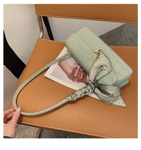 Détail du sac baguette vert clair à motif crocodile avec foulard en soie sur chaise