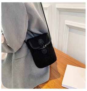 Detail of a black plush crossbody bag with horn buckle on a model wearing a grey blazer