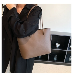 Detail of dark brown leather tote bag with lychee texture worn by a model in black coat