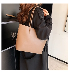Detailed view of large brown pebble leather tote bag carried on shoulder with black coat