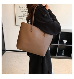 Detail of dark brown tote bag with pebble leather texture worn by model with black coat
