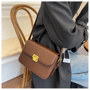 Detail of dark brown leather crossbody bag with golden square metal lock and strap