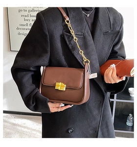 Detail of a brown matte leather shoulder bag with a gold chain strap and square twist lock