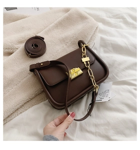 Detail of dark brown leather square bag featuring a gold geometric clasp and metal chain