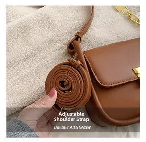 Detail of brown faux leather saddle bag with gold hardware and adjustable shoulder straps