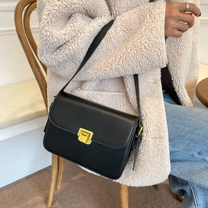 Classic black leather crossbody bag with gold buckle on model in beige coat