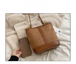 Close-up of brown suede bucket bag with leather accents and gold hardware next to phone