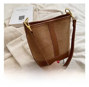 Detail of caramel suede bucket bag with gold hardware on white textured background