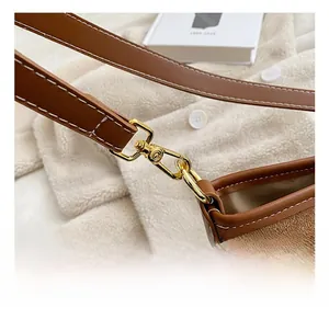 Detail of golden metal swivel hook and white stitching on brown suede bucket bag