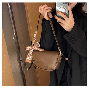 Detail of brown saddle bag with wavy flap design and checkered bow scarf decoration