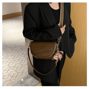 Detail of a dark brown leather saddle bag with a decorative bow and gold hardware