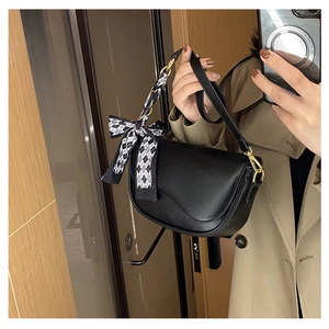 Detail of black saddle bag with metallic chain and black and white checkered bow ribbon