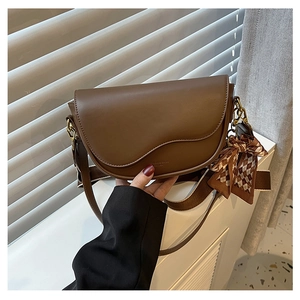 Detail of a dark brown saddle bag featuring a wavy flap design and elegant plaid scarf